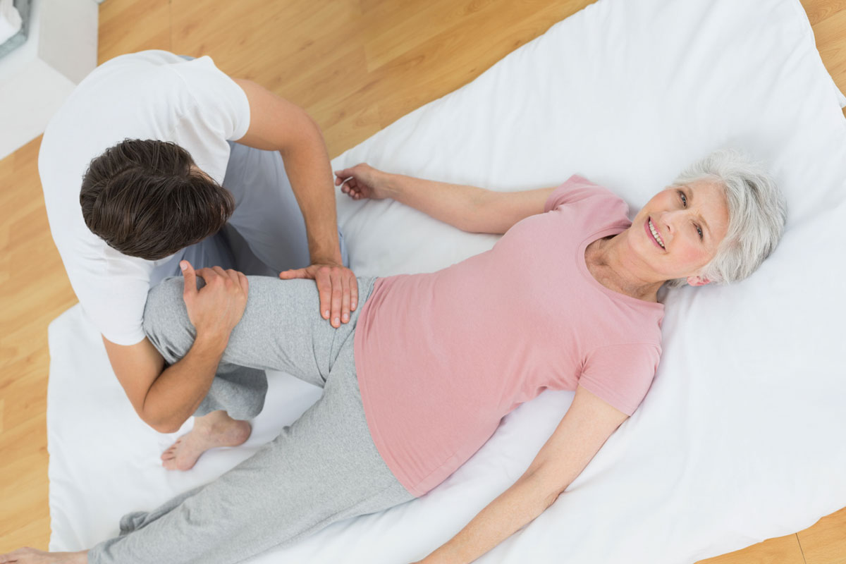 Therapeut mobilisiert im Liegen das Bein einer älteren Patientin
